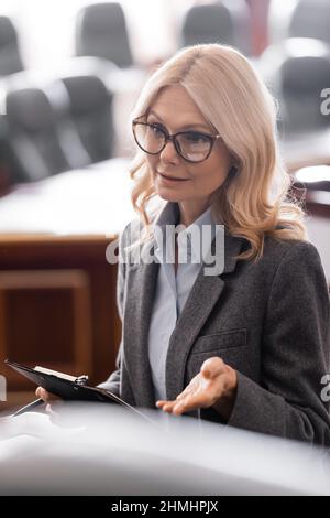 blonde middle aged advocate with clipboard talking in courtroom Stock Photo