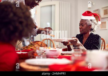 Grandfather Carving And Serving As Multi Generation Family Enjoy Eating Christmas Meal At Home Stock Photo