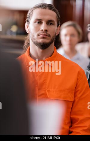 bearded man in jail uniform looking at camera near blurred african ...