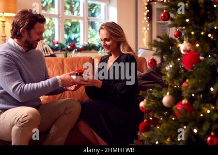 Loving Couple Opening Gifts Around Christmas Tree At Home Stock Photo