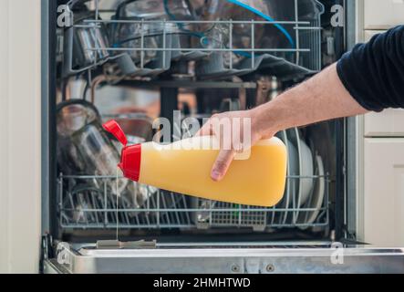 arm of a man holding a bottle of detergent and pouring it into the dishwasher Stock Photo