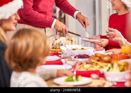 Grandfather Carving Turkey As Multi-Generation Family Sit Down To Eat Christmas Meal Together Stock Photo