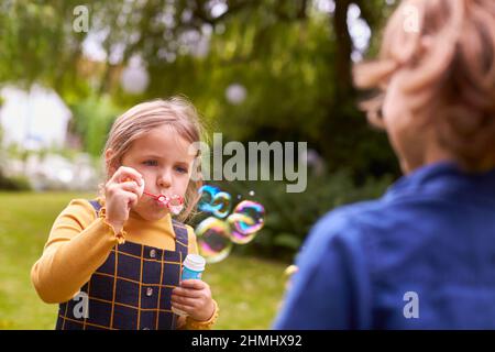 Boy And Girl Having Fun In Garden Blowing Bubbles Together Stock Photo