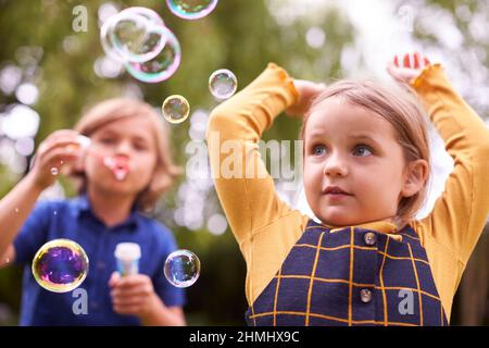 Boy And Girl Having Fun In Garden Blowing Bubbles Together Stock Photo
