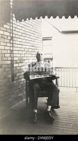 Antique circa 1910 photograph of an elderly man reading a newspaper in a rocking chair on his front porch. 'The News' was a newspaper in Dayton, Ohio. SOURCE: ORIGINAL PHOTOGRAPH Stock Photo