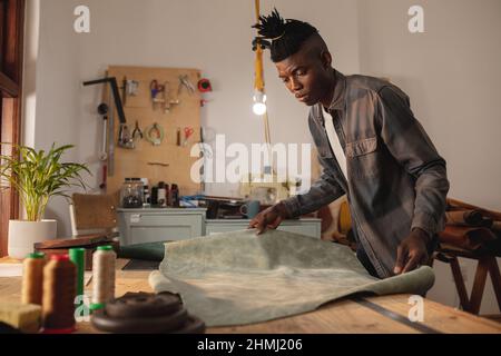 African american young craftsman keeping leather on workbench while working in workshop Stock Photo