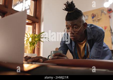 African american young craftsman using laptop at table in leather workshop Stock Photo