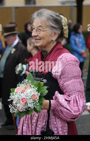 A woman wearing a traditional dirndl and carrying a bunch of flowers participates in the Oktoberfest parade in Munich Stock Photo