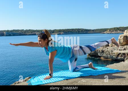 middle-aged fitness woman outdoors in front of the sea does yoga stretching exercises. Stock Photo