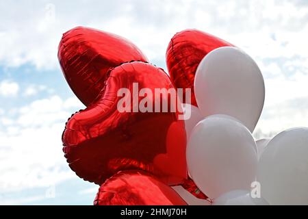 Munich, Germany. 10th Feb, 2022. Balloons in the shape of red hearts hang on a string next to a wedding party. Credit: Katrin Requadt/dpa/Alamy Live News Stock Photo