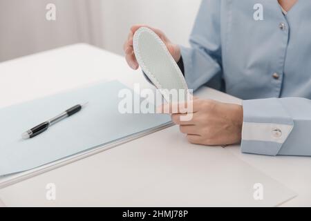 Doctor holding an insole while sitting at a table. Orthopedist tests the medical device. Orthopedic insoles. Foot care. Flat Feet Correction Stock Photo