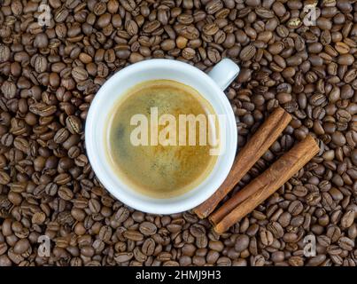 A coffee in white cup surrounded by coffee beans and cinnamon sticks Stock Photo
