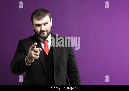Pointing gesture. You. A man in a suit points his finger forward on a gray background. Finger on the camera. Stock Photo