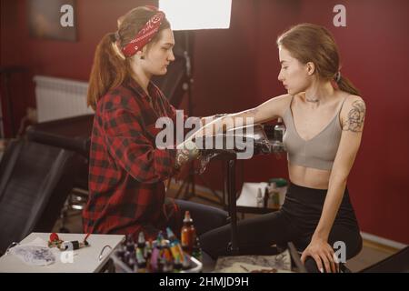 Tattoo artist helping client to put her arm on the pillow Stock Photo