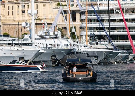 A large boat enters the port, the girl on the deck is talking on the phone, A lot of huge yachts are in port of Monaco on background, Monte Carlo Stock Photo
