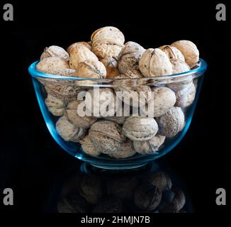 Whole solid walnuts in a glass bowl on black reflective background Stock Photo