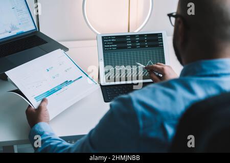 Anonymous male broker analyzing financial diagrams during work on tablet and laptop Stock Photo