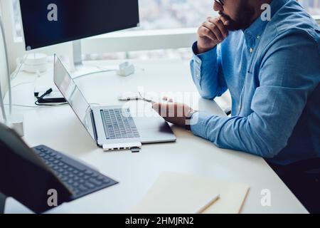 Crop concentrated young bearded businessman using smartphone while working in office with various gadgets Stock Photo