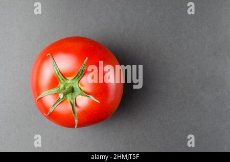 Bright, red and ripe tomato on dark grey background.Close up. Stock Photo