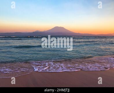 Mount Agung active volcano in Nusa Penida, Bali island, Indonesia. Amazing sunset. Sand beach. High waves with foam spread on the coast.