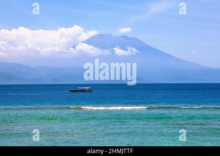 Mount Agung active volcano covered by clouds in Nusa Penida, Bali island, Indonesia. Traditional fishing boats called jukung on the white sand beach.