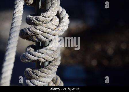 Against a dark colored background a thick natural fiber rope wrapped around a metal pole with space for text in landscape format Stock Photo