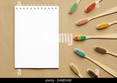Multiple multicolor bamboo toothbrushes are lying on craft eco paper with notepad. Copy space, top view. Stock Photo