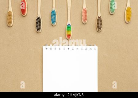 Multiple multicolor bamboo toothbrushes are lying on craft eco paper with notepad. Copy space, top view. Stock Photo
