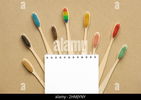 Multiple multicolor bamboo toothbrushes are lying on craft eco paper with notepad. Copy space, top view. Stock Photo