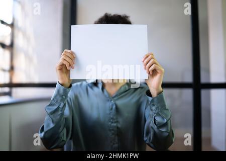 Businesswoman Holding Empty Paper In Front Of Face At Desk In Office Stock Photo