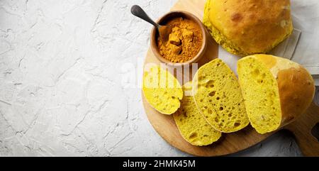 Turmeric bread, two tumeric bread rolls, one cut into slices on wooden cutting board. White plaster background, top view, space for text. Stock Photo
