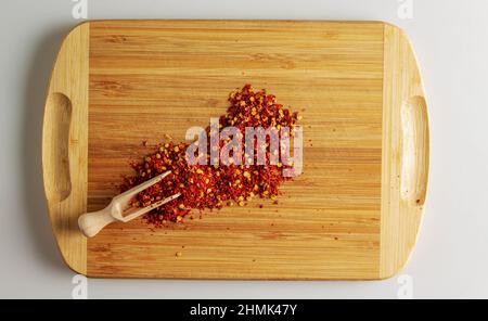 Spoon with crushed dry red chili peppers on a wooden kitchen board. Top view. Stock Photo