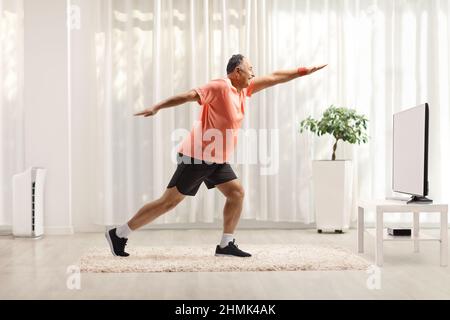 Full length shot of a mature man in sportswear exercising and stretching in front of tv at home Stock Photo