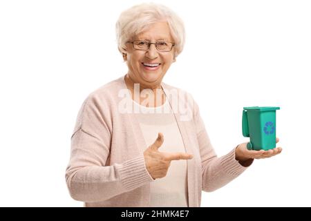 Smiling elderly woman holding a small recycling bin on her hand and pointing isolated on white background Stock Photo