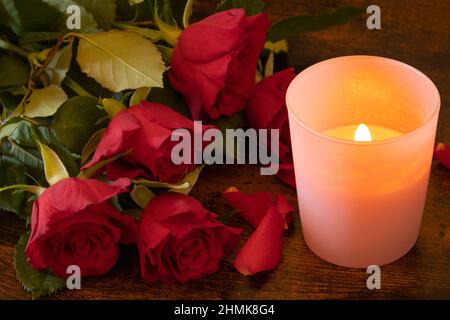 bouquet of red rose with petals and a candle on a wooden background Stock Photo