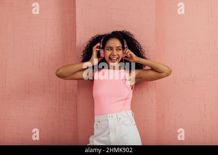 Beautiful woman with curly hair listening to music by pink headphones wearing casual clothes having fun Stock Photo