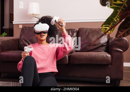 Woman with curly hair wearing VR helmet while sitting in living room at sofa Stock Photo