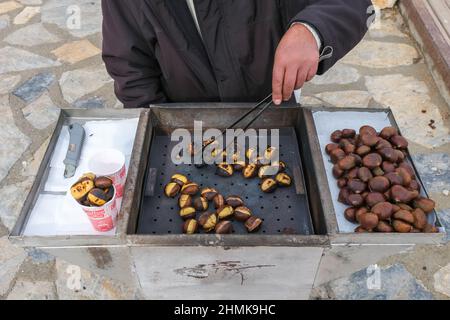 Man hand selling Traditional chestnuts on a street, Freshly cooked chestnuts from turkısh cuisine, Street market, Turkish cuisine and cooking concept. Stock Photo