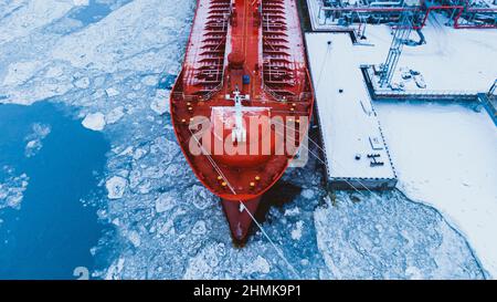 Oil shipment on big red tanker from terminal pumping system on water covered with thick layer of broken ice in frosty winter aerial view Stock Photo