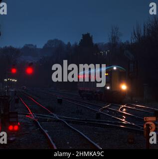 London midland Bombardier class 172 train with its headlights glinting on the track and red signals at Stourbridge junction on a dark wet night Stock Photo