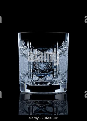 Empty crystal whiskey glass on black reflective surface with rim light Stock Photo