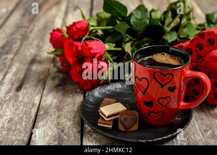 Bouquet of red roses, cup of coffee, gift box and chocolates candies on wooden table. Romantic concept for Valentine's day. Stock Photo