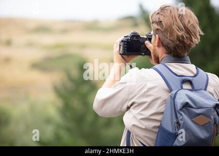 young man trekking among trees and taking pictures Stock Photo
