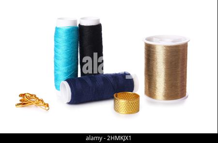 Different thread spools, thimble and safety pins on white background Stock Photo