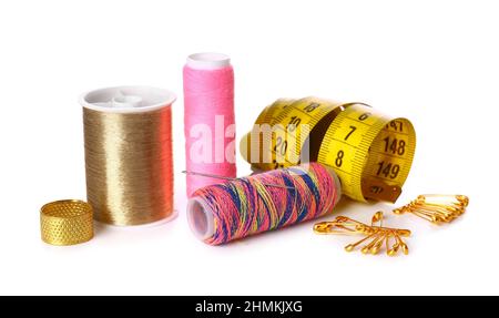 Different thread spools, thimble, measuring tape and safety pins on white background Stock Photo