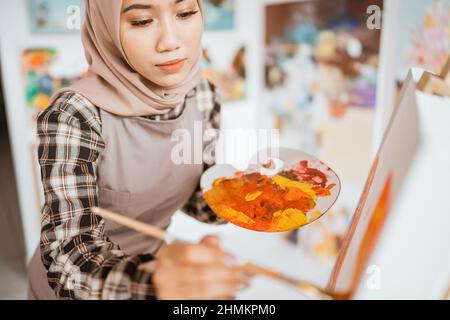 concentrated asian muslim female artist painting on canvas Stock Photo