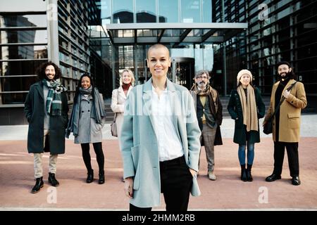 Leading business woman standing out from a group of business people while standing together in the financial district. Stock Photo