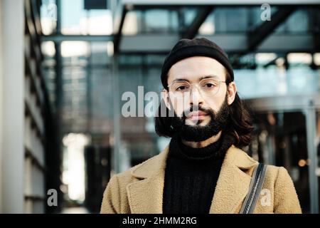 Man looking at the camera with a serious expression on his face while standing against an office building. Stock Photo