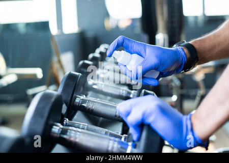 close up shot of hands with gloves sanitizing dumbbells at gym due to coronavirus - concept of covid-19 disinfecting, protection from virual infection Stock Photo