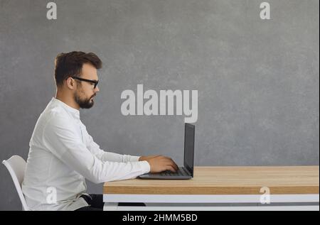 Portrait of a side view of a man at a table with a laptop prints, on a black background Stock Photo